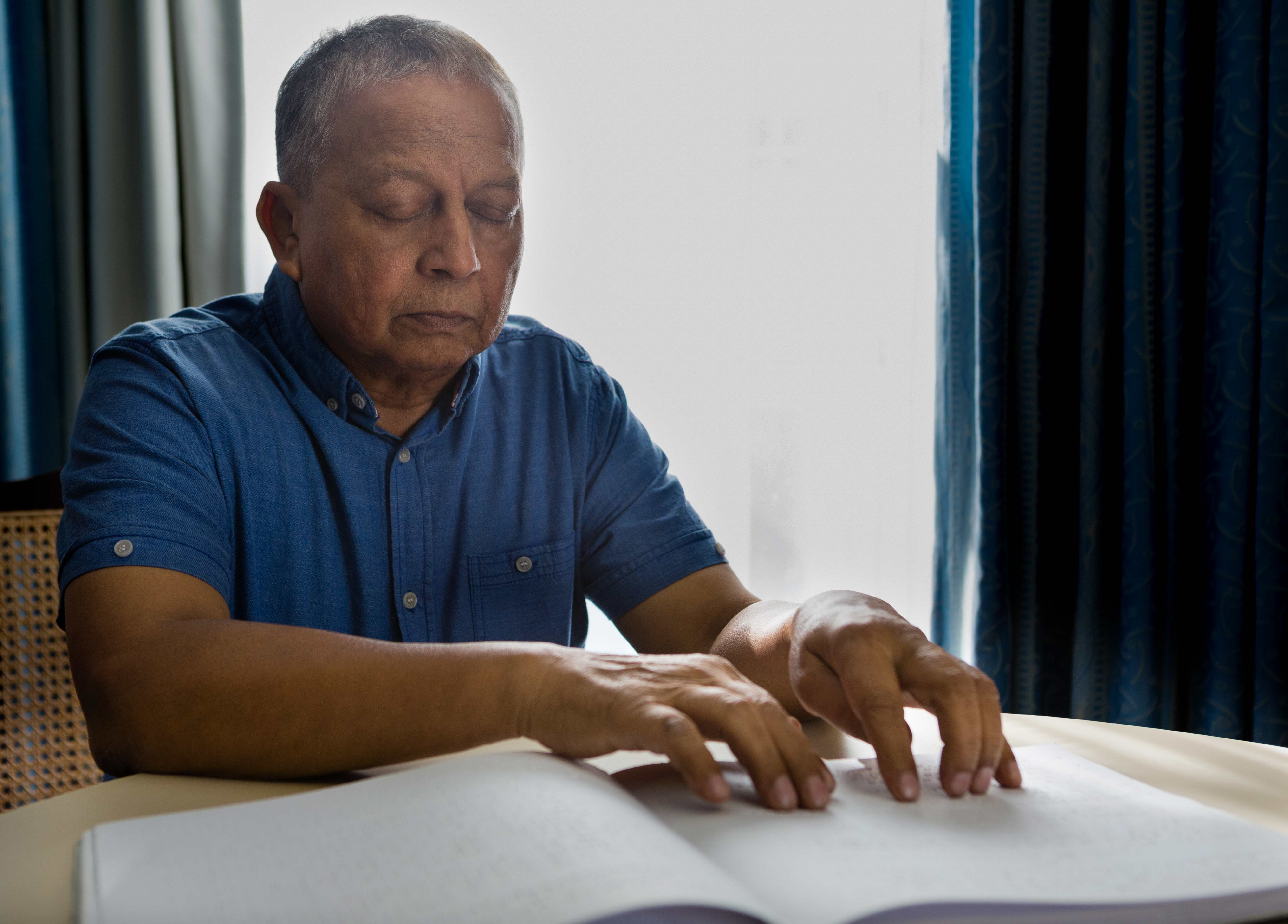 man reading braille book in home