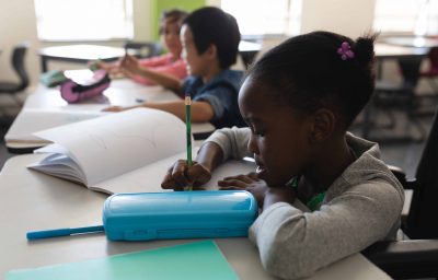 disabled schoolgirl studying and sitting at desk in classroom of elementary school