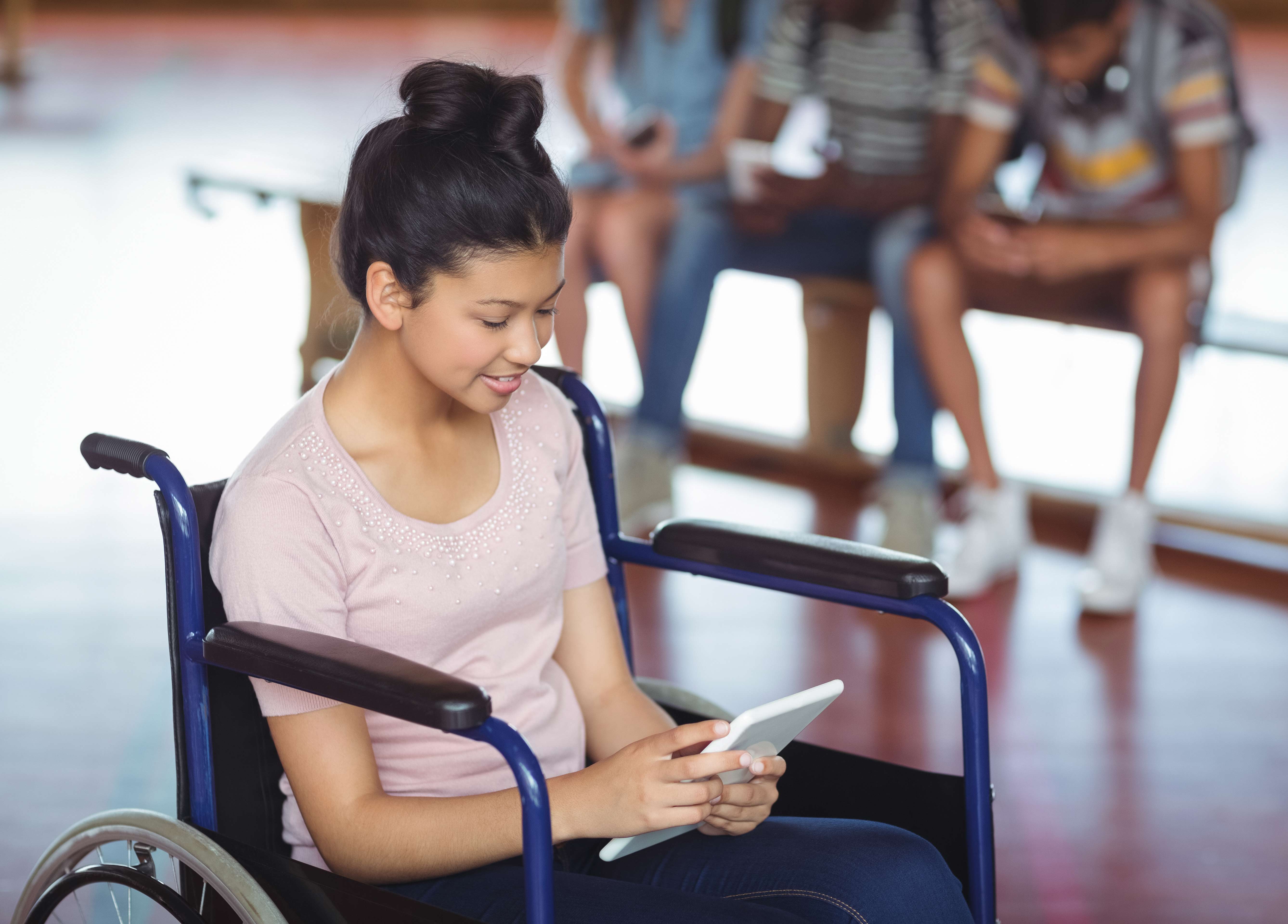 Disabled schoolgirl using digital tablet with classmates in background