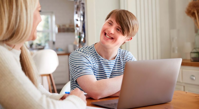 Downs Syndrome Man Sitting With Tutor Using Laptop