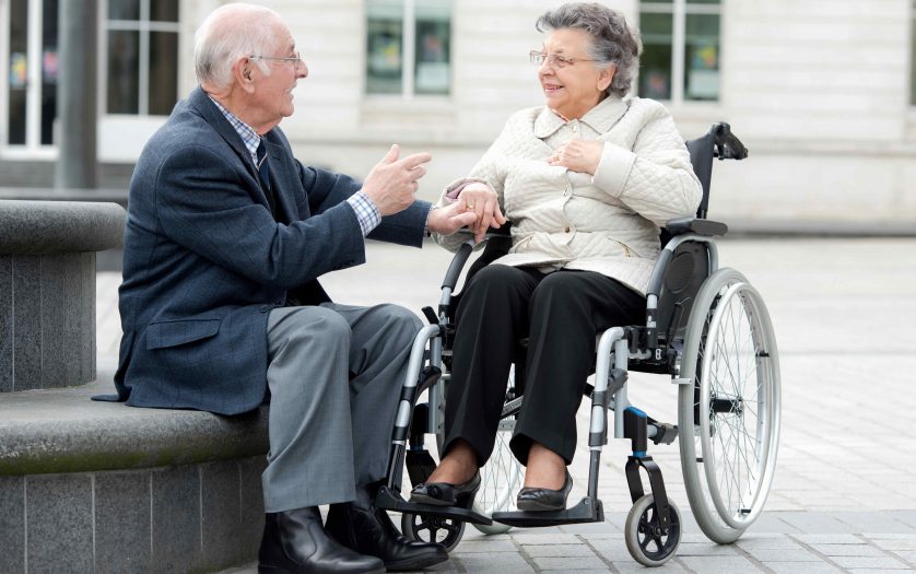 man and woman sitting in wheelchair talking outdoors