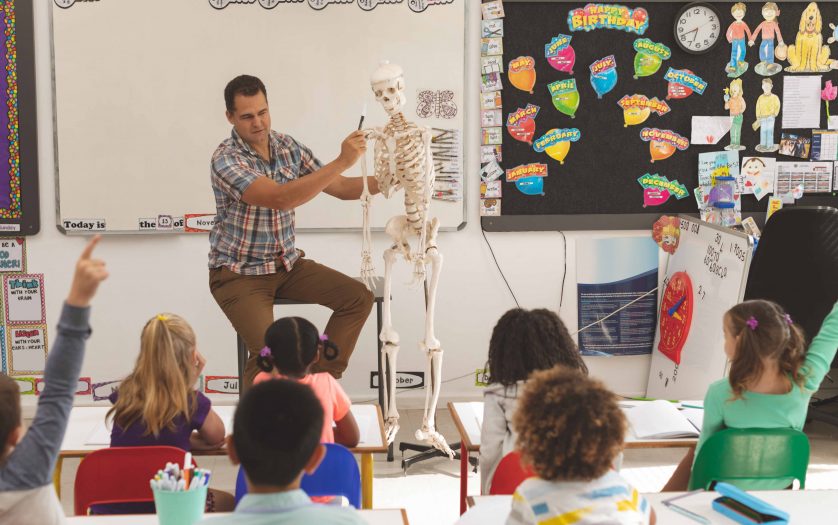 Teacher explaining human skeleton in classroom at school