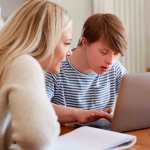 Downs Syndrome Man Sitting With Tutor Using Laptop