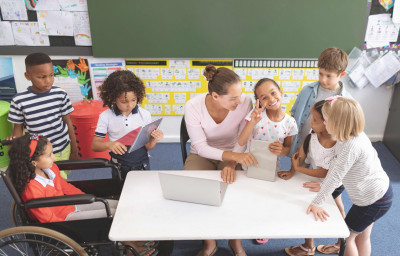 schoolgirl looking at the camera while his classmates and her teacher are around a table