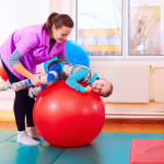 cute kid with disability has musculoskeletal therapy by doing exercises in body fixing belts on fit ball