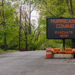 Hurricane Coming Evacuate Now warning information sign on trailer with LED face on suburban street lined with trees
