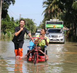 A volunteers help disabled man with his wheelchair walk through flood