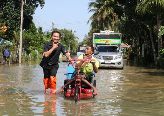 A volunteers help disabled man with his wheelchair walk through flood