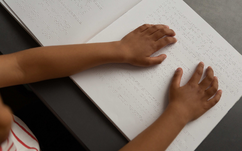 Blind schoolboy hands reading a braille book in classroom