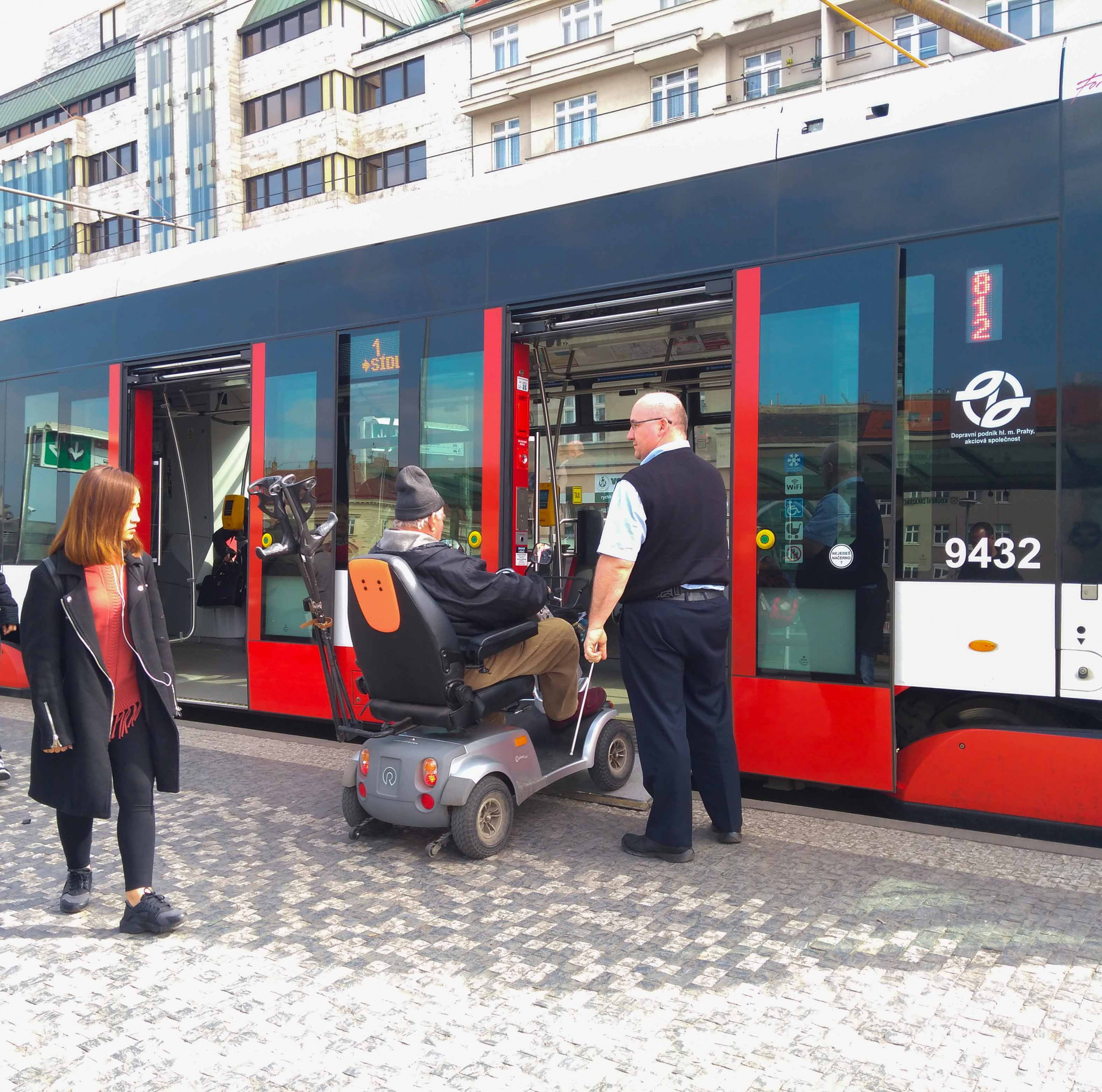 A tram driver helps a person with disabilities enter a tram in an electric wheelchair