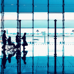 Silhouettes of people with luggage walking at airport.