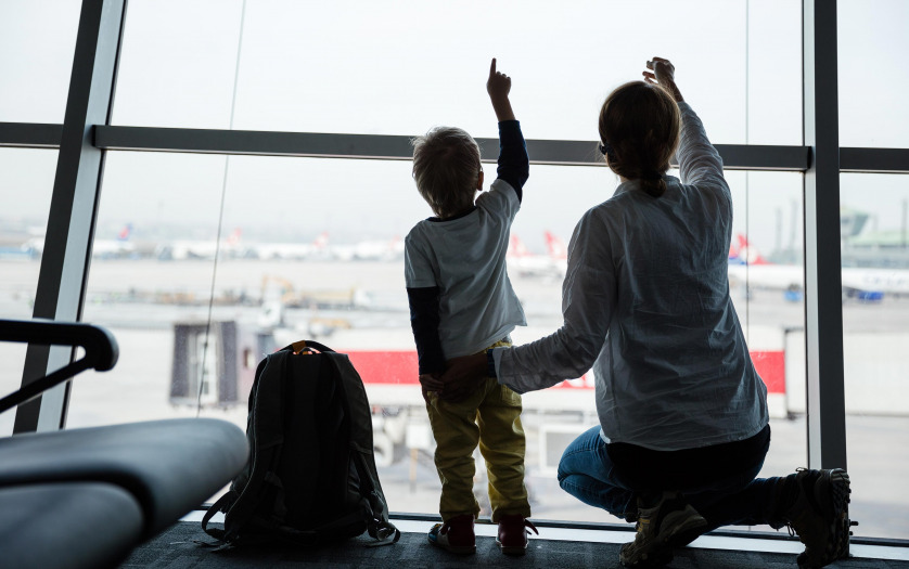 Mother and son pointing to taking off airplanes while looking through window in airport