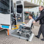 Side view of taxi driver assisting man on wheelchair to board van outside building
