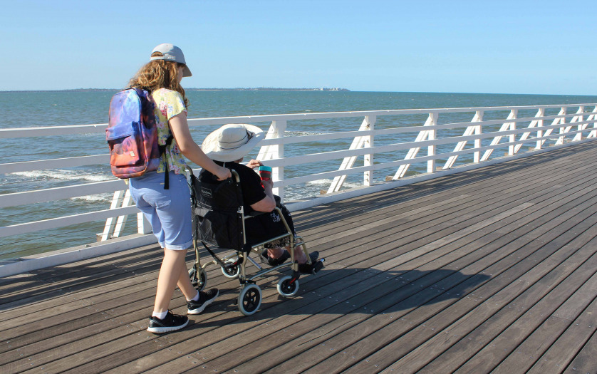Teenage girl pushing her grandmother in a wheelchair along the pier