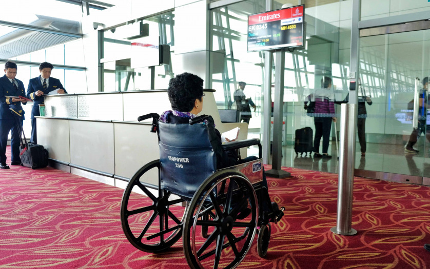 Elderly female passenger sitting on wheelchair awaiting to be boarded into a flight at an airport terminal gate.