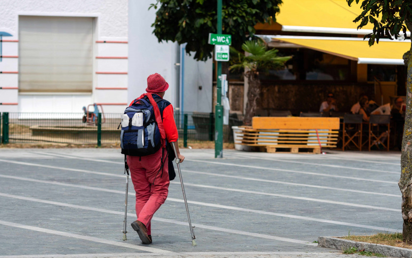 A woman with crutches and a backpack goes along the sidewalk.