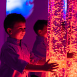Child in sensory stimulating room, interacting with colored lights bubble tube lamp