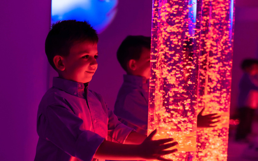 Child in sensory stimulating room, interacting with colored lights bubble tube lamp