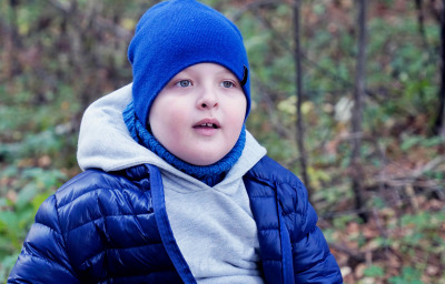 child autistic in blue hat and blue jacket playing with wilted leaves in autumn Park