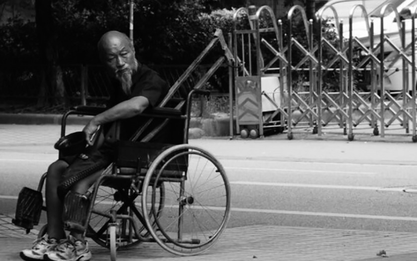 An elderly man in wheelchair patiently waiting for his ride.