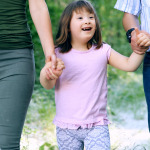 Beautiful little girl with down syndrome walking with parents