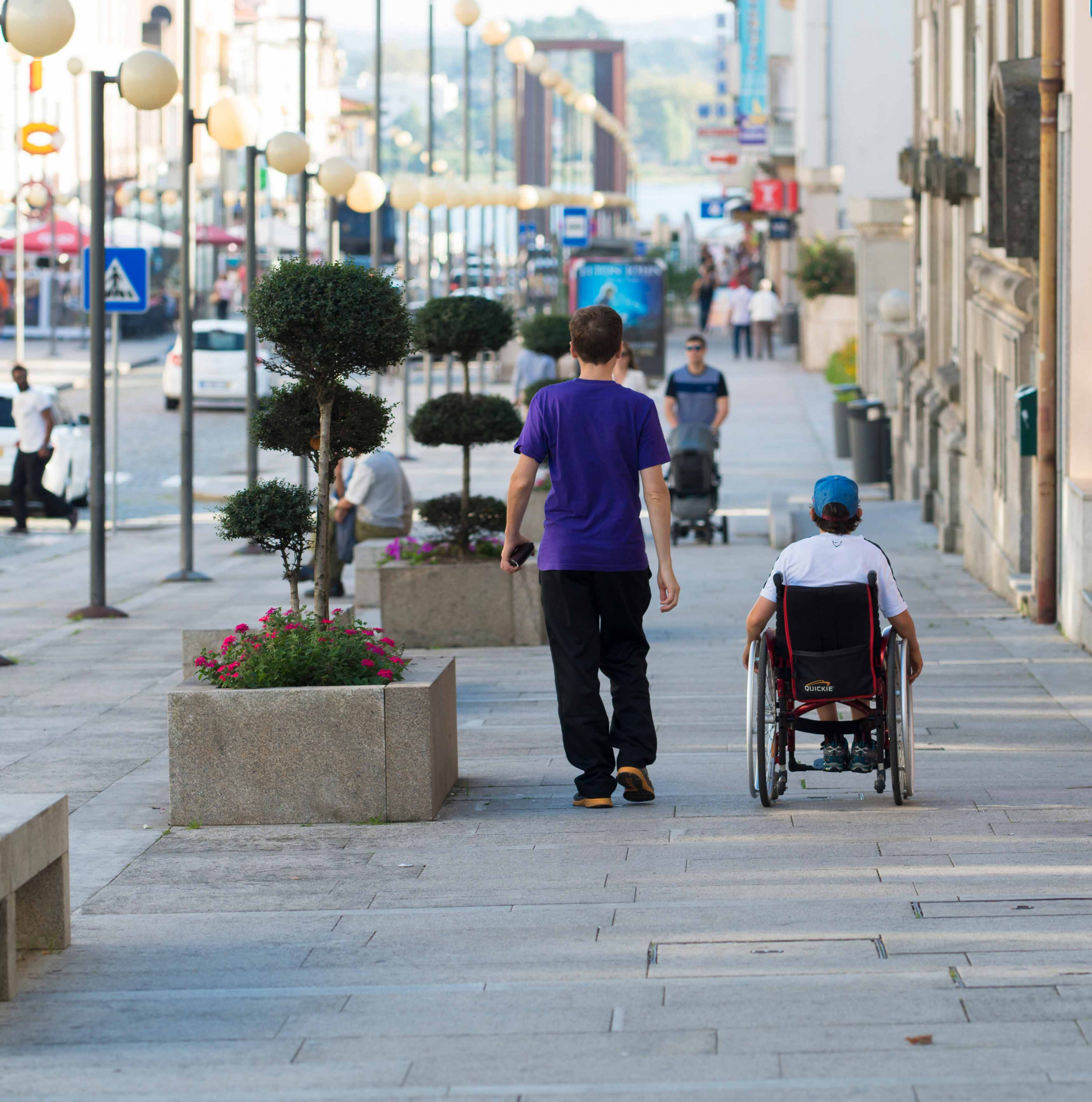 A man with a child in a wheelchair walking in the street