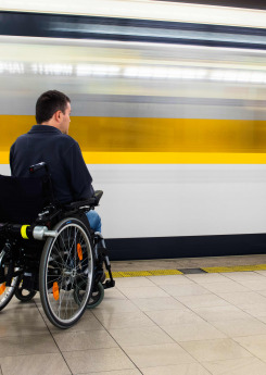 Back view of man in his electric wheelchair at underground platform waiting for train with motion blur of passing train in the background