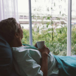 Senior man on a hospital bed alone in a room looking through the hospital window