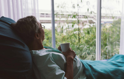 Senior man on a hospital bed alone in a room looking through the hospital window