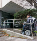 Man in a wheelchair using a ramp next to stairs.