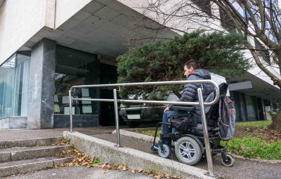 Man in a wheelchair using a ramp next to stairs.