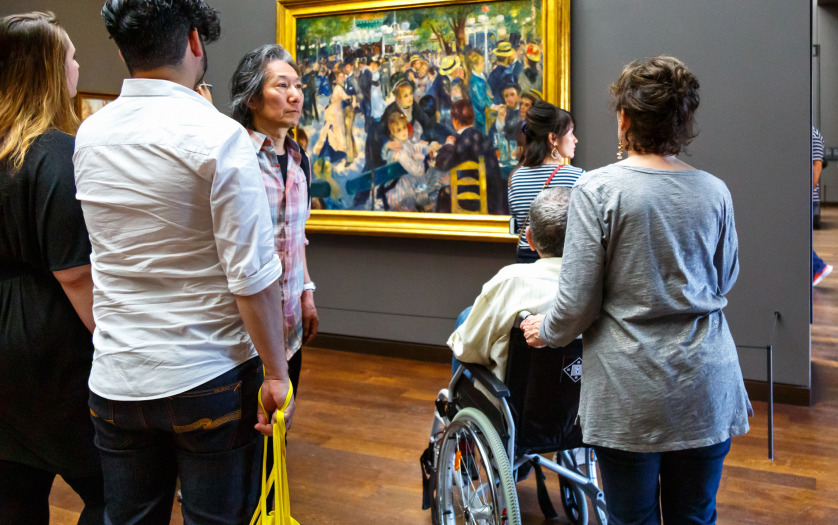 Visitors in art museum Orsay (Musee d'Orsay). Elderly man is sitting in wheelchair looking at artwork of impressionist artist Renoir.