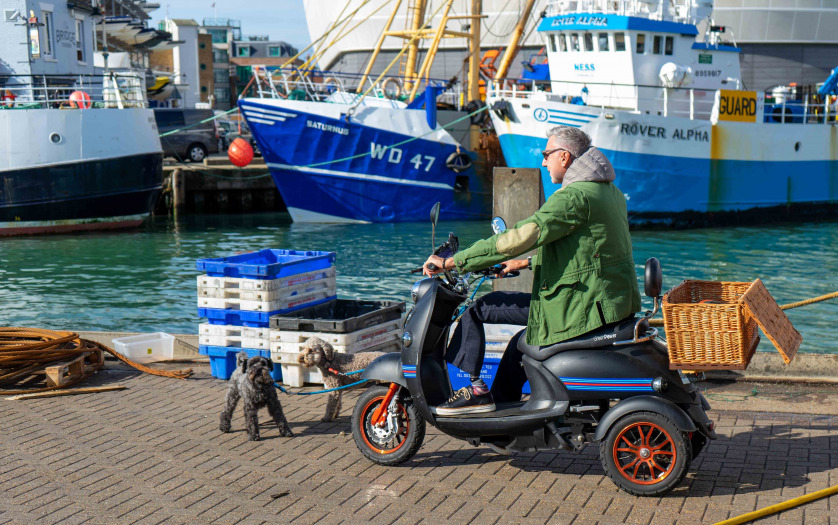 UK a middle aged man on a mobility scooter taking his dog for a walk on the quayside or dock