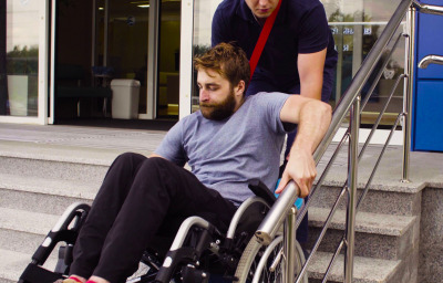 A man helping to move down the stairs to a disabled person in a wheelchair