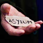Closeup of the hand of an old man with a piece of paper with the word asylum, with a dramatic effect