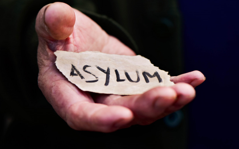 Closeup of the hand of an old man with a piece of paper with the word asylum, with a dramatic effect