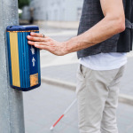 blind man with white cane at pedestrain crossing in city.
