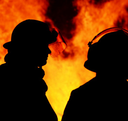 A striking silhouette image of two firemen called to an Australian bushfire blaze that started at night time. The men are discussing their plans for controlling the blazing flames.