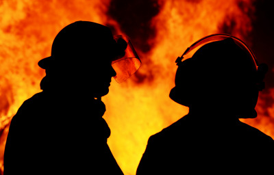 A striking silhouette image of two firemen called to an Australian bushfire blaze that started at night time. The men are discussing their plans for controlling the blazing flames.