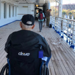 An elderly man rolling on the cruise ship deck in his wheechair.