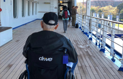 An elderly man rolling on the cruise ship deck in his wheechair.