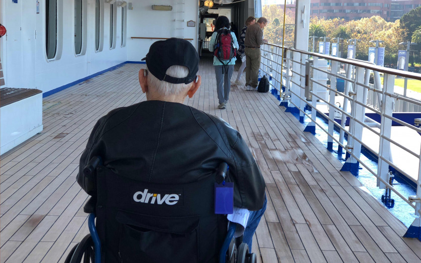 An elderly man rolling on the cruise ship deck in his wheechair.