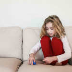 a child with autism sitting alone on a couch, stacking toys instead of playing with them in the usual manner
