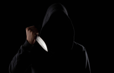 A dangerous hooded man standing in the dark and holding a shiny knife