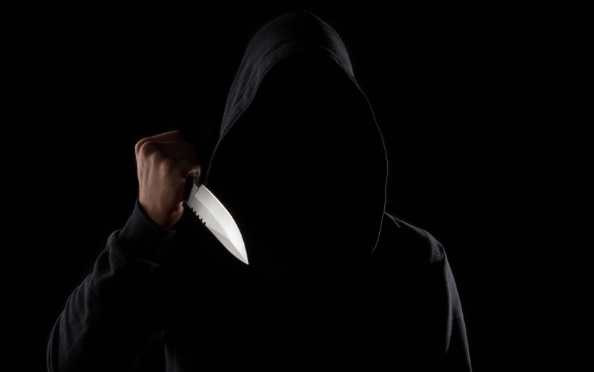 A dangerous hooded man standing in the dark and holding a shiny knife