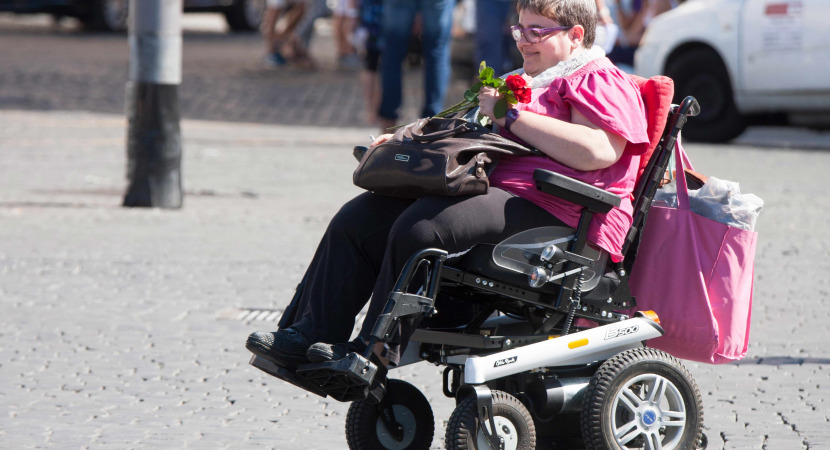 A woman with a disability through the city with his means of transport. She keeps some roses in her hand.