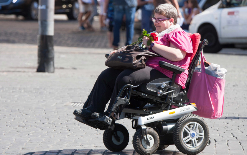 A woman with a disability through the city with his means of transport. She keeps some roses in her hand.