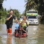 A volunteers help disable man with his wheel chair walk through flood and he still smile in Southern, Thailand.