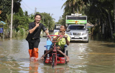 A volunteers help disable man with his wheel chair walk through flood and he still smile in Southern, Thailand.