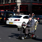 Elderly man drive mobility scooter through the London street.